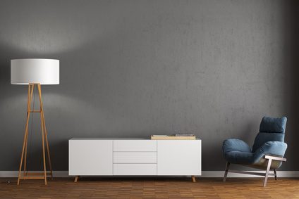 Sessel, Sideboard und Stehlampe vor grauer Wand